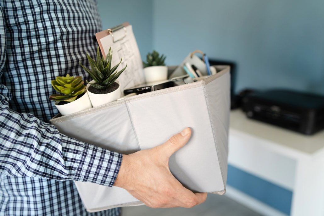 Man holding a box of desk items including plants, papers, and a clipboard.