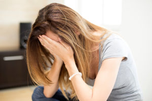 Woman sitting down with her hands on her face.