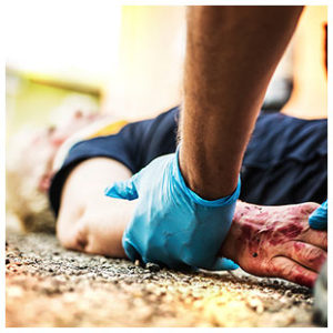 Someone in a surgical glove is holding the arm of a badly injured woman laying on the asphalt.