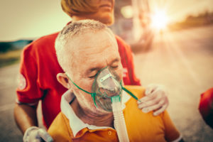 A paramedic is pushing an old man wearing an oxygen mask.