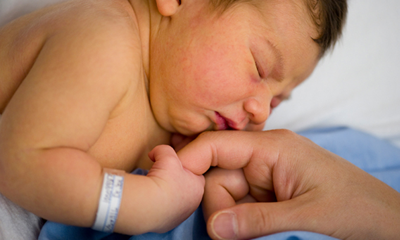 A newborn baby is gripping someone's finger.
