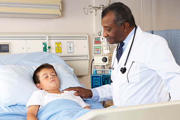 Doctor looking in on a little boy sleeping in a hospital bed.