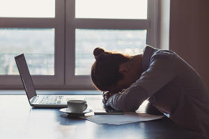 A woman with her head on the table and a laptop sitting in front of her.