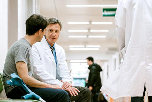 A doctor siting in a hospital hall talking to a patient.