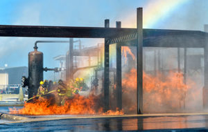 Firefighters putting out a large fire with a rainbow in the background.