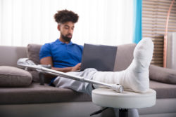 Man is sitting on the couch on the computer with his leg propped up in a cast.
