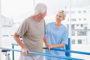 A woman in scrubs is helping an older man with his hip rehab.