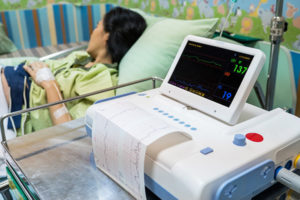 A woman lying in a hospital bed next to an EKG machine.