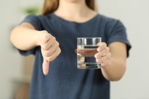 A woman holding a glass of water in one hand and the other hand is a thumbs down.