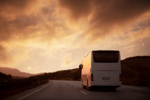 A charter bus is driving on the freeway as the sun sets.