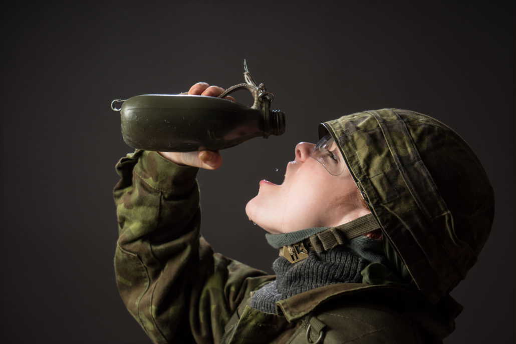 A woman in a military uniform drinking from a canteen.