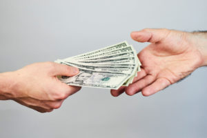 Five dollar bills are being exchanged between two hands.
