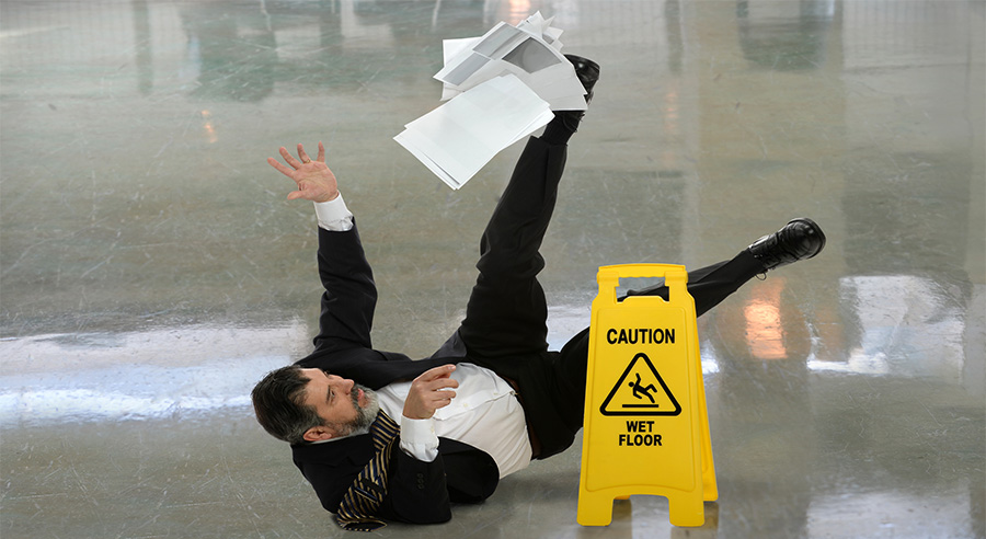 A man has fallen and dropped papers next to a yellow "wet floor" sign.