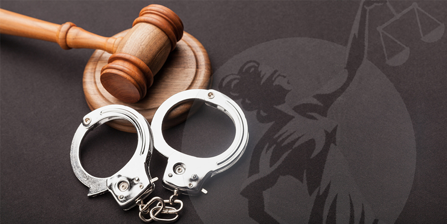 A wood gavel and silver handcuffs on top of a black sheet with Lady Justice on it.