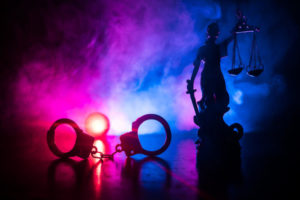 Handcuffs on the floor and a statue holding a balanced scale in a dark room with colorful fog.