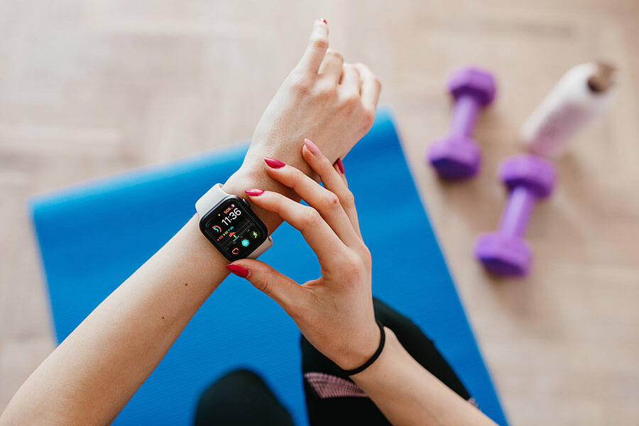 A woman programming her smartwatch with a yoga mat in the background.