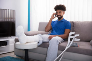 A guy is sitting on the couch talking on the phone while his leg is propped up in a cast.