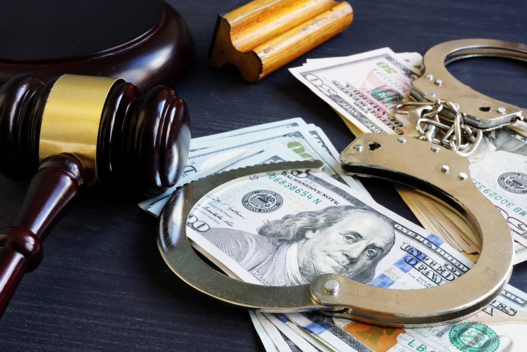Cash on a table with a gavel and handcuffs.