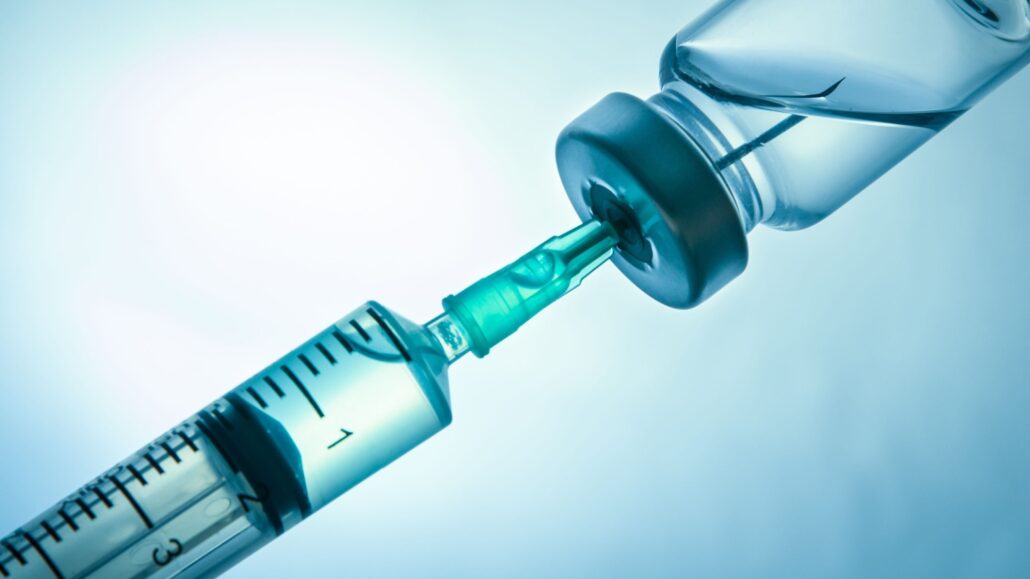 Closeup of a syringe injecting a vaccine vial.