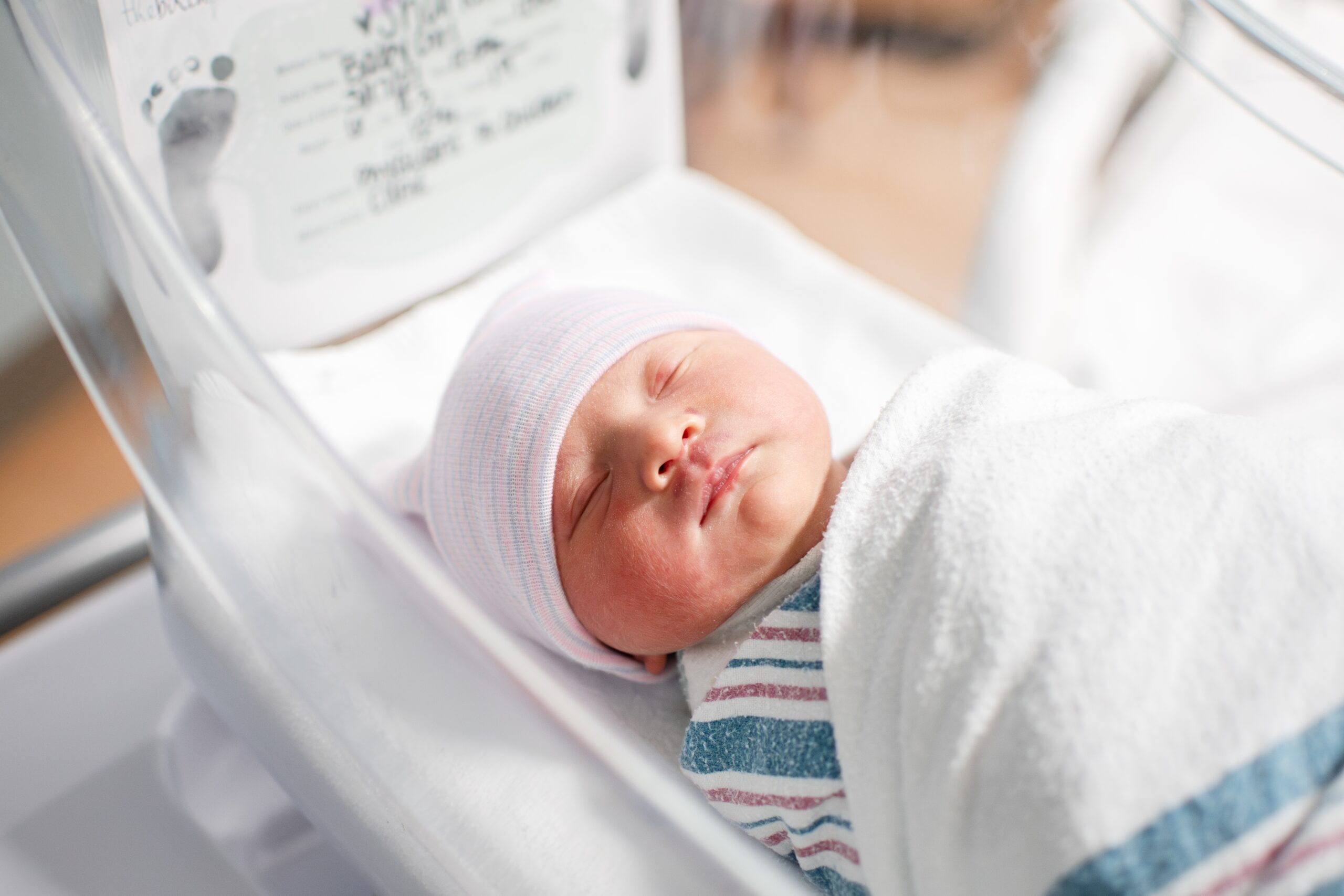 A newborn baby lays swaddled in a bassinet in a hospital nursery